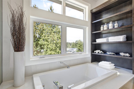 A white drop in tub fitted with wooden shelves with stacked towels and white seashells sits beneath...