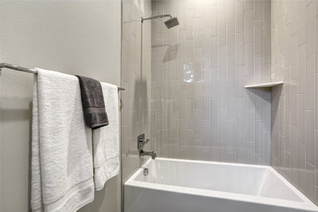 Bath tub area with shiny grey tiles and white towels.