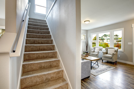 Foyer staircase lined with beige carpet runner and living room view.の写真素材