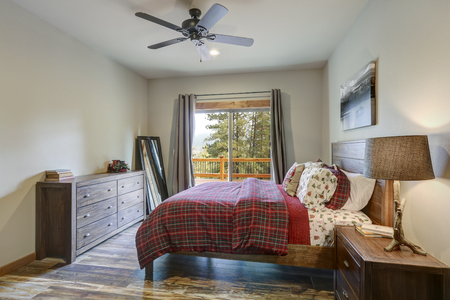 Restful country bedroom furnished with wooden master bed, dark gray dresser and view of spacious deckの写真素材