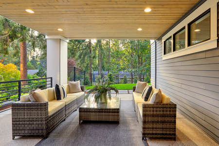 Luxury modern house exterior with covered patio boasting stone fireplace and cozy rattan furniture.の写真素材