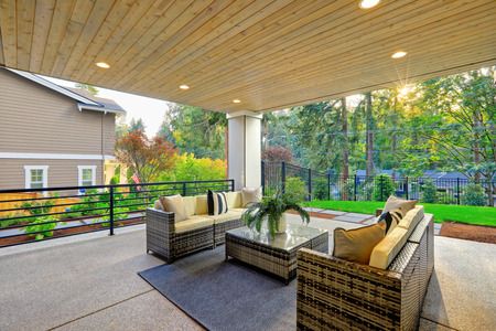 Luxury modern house exterior with covered patio boasting stone fireplace and cozy rattan furniture.の写真素材