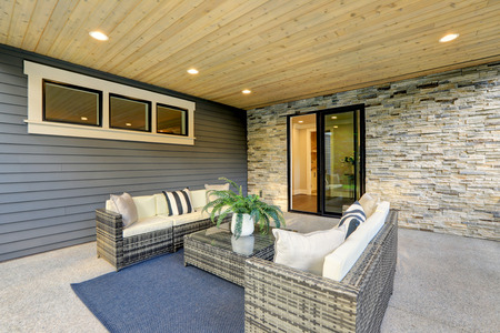 Luxury modern house exterior with covered patio boasting stone fireplace and cozy rattan furniture.の写真素材