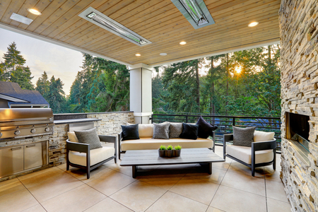 Luxury modern house exterior with covered patio boasting stone fireplace and cozy rattan furniture.の写真素材