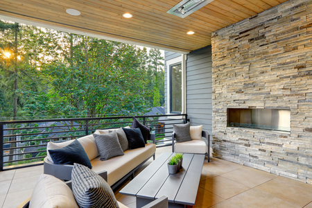 Luxury modern house exterior with covered patio boasting stone fireplace and cozy rattan furniture.の写真素材