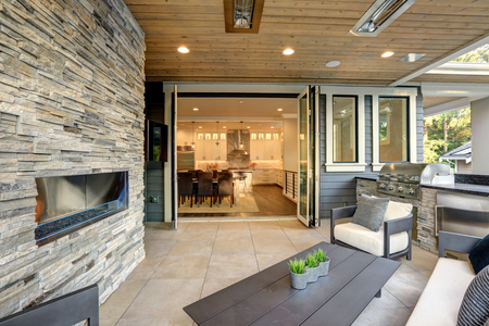 Luxury modern house exterior with covered patio boasting stone fireplace and cozy furniture.の写真素材