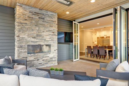 Luxury modern house exterior with covered patio boasting stone fireplace and cozy rattan furniture.の写真素材