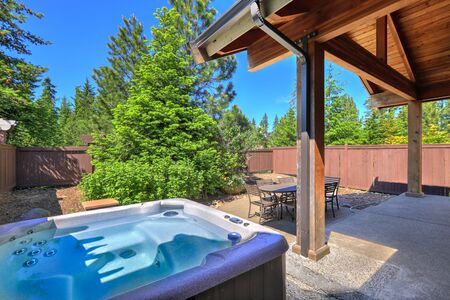 Small fenced  back yard space with dining room table  and hot tub surrounded by treesの写真素材