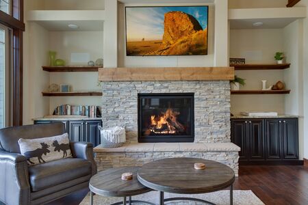 An absolute beautiful luxury living room with huge vaulted  ceiling, fire place, harwood floor, amazing furniture, and lots of windows and doors. Solid wood rustic modern dining room table. SHelves around fire place with TV above.の写真素材