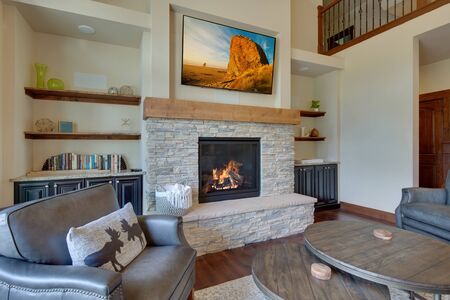 An absolute beautiful luxury living room with huge vaulted  ceiling, fire place, harwood floor, amazing furniture, and lots of windows and doors. Solid wood rustic modern dining room table. SHelves around fire place with TV above.の写真素材