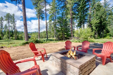 Huge open to nature Back yard with fire pit , amazing patio and red chairs near newly bild luxury real estate home with forest biew and green grass.の写真素材