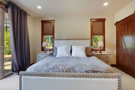 Beautiful large luxury new bedroom with great design, beige, grey and white tones, TV bove dresser, rich wooden doors, window blinds and grey carpet. Cozy and practicle. Expensive furniture. Doors open to back yard patio.の写真素材