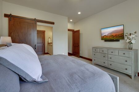 Beautiful large luxury new bedroom with great design, beige, grey and white tones, TV bove dresser, rich wooden doors, window blinds and grey carpet. Cozy and practicle. Expensive furniture. Doors open to back yard patio.の写真素材
