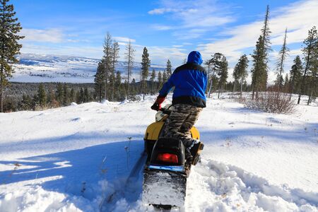 Man riding snowmobile in the mountains with pine trees and houses.の写真素材