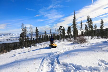 Man riding snowmobile in the mountains with pine trees and houses.の写真素材