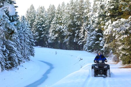 Man riding snowmobile or fourwheeler on the country side trail near water canal.の写真素材