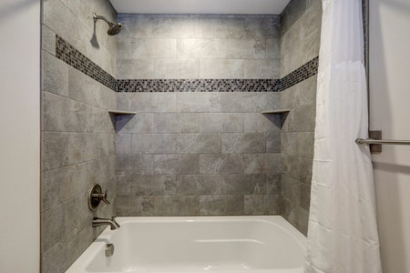 WHite new tub details with curtain and grey tiles.