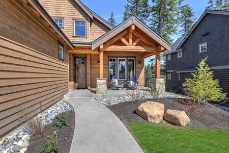 Cedar new house exterior with covered entrance and driveway with green grass and pine trees.の写真素材