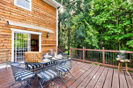 Cedar wooden large American house extrerior with green nature and cozy private deck with metal chairs and table sent up for lunch or picnic.の写真素材