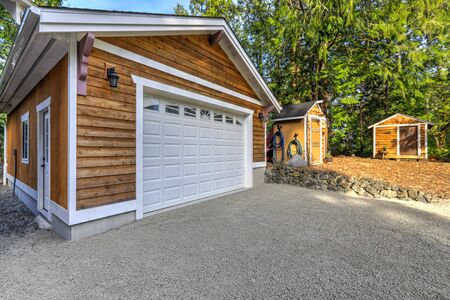 Detached free standing large garage or shop natural brown tone with white trim and green summer nature.の写真素材