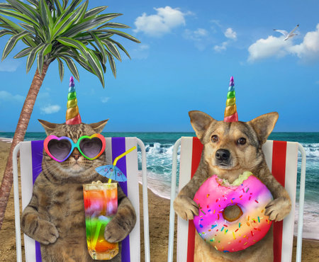 The dog with a donut and the cat with a glass of colored cocktail are sitting under the palm tree on...