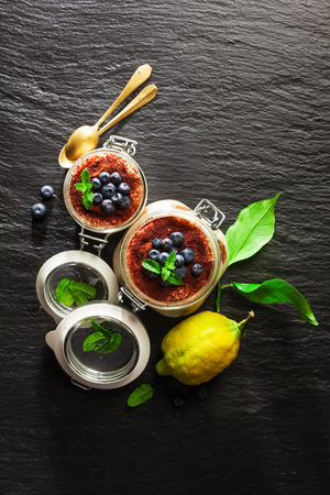 Lemon tiramisu. An alternative summer Italian dessert covered with blueberries with Savoyardi biscuits and coffee on black stone backgroundの写真素材