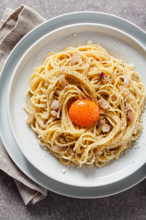 Pasta Carbonara on white plate with parmesan, red wine and yolkの写真素材