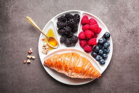 Fresh hot Croissant with ripe berries and maple syrup on a white plate on a gray background. Healthy Breakfastの写真素材