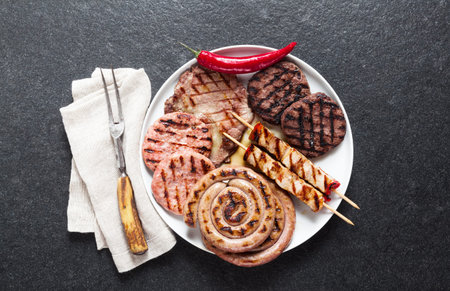 Meat barbecue party. Meat grilled on a plate, basil leaves, tomatoes and fork for meat