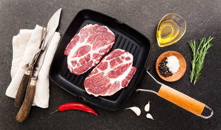 raw steak in a frying pan for the grill on stone background  with cutting Cutlery for slicing and spicesの写真素材