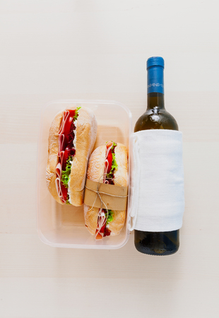 A Panini sandwich with ham, tomatoes and fresh lettuce leaves and a Bottle of white wine. wooden background, copy space. In a plastic box on the kitchen tableの写真素材