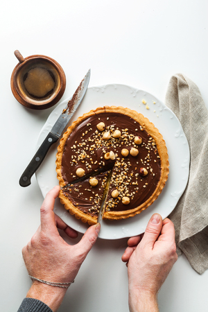 Italian walnut cake crostata with chocolate and hazelnuts. and coffee . men's hands take a cut pieceの写真素材