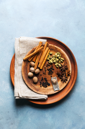 Spice collection on the plate : cinnamon sticks, nutmeg, anise, cardamom, black pepper, cloves. on blue table background. の写真素材