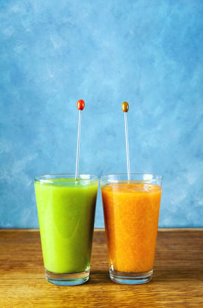 Freshly blended fruit smoothies of various colors and tastes in glass  in wooden tray. Yellow, green. on wooden table and blue backgroundの写真素材