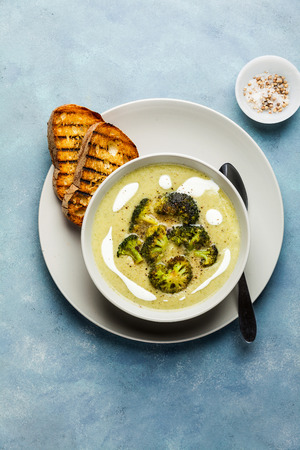broccoli cheese soup and fresh grilled bread with sour cream and black pepper on blue backgroundの写真素材