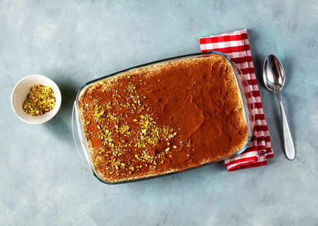 traditional Italian dessert with coffee, cocoa and mascarpone cheese Tiramisu cake in an oven pan on a blue table . sprinkled with pistachioの写真素材