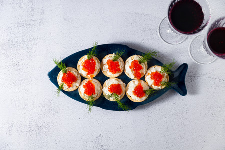 appetizer of red caviar and cheese with dill in a plate in the shape of a fish on a stone background and two glasses of red wineの写真素材