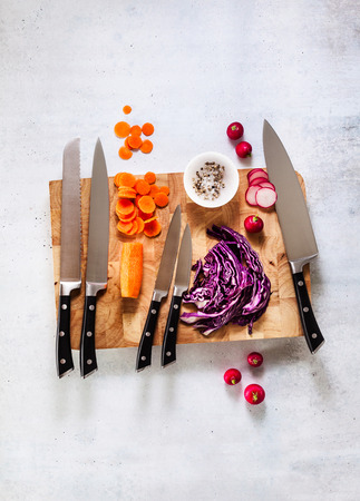 set of new professional kitchen knives on a wooden cutting board and vegetablesの写真素材