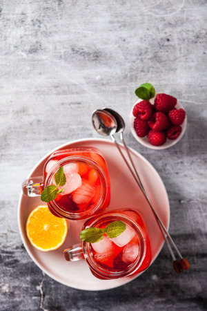 summer refreshing drink with ice and fresh ripe berries. raspberries and blackberries with citrus on a stone background table in glass jars with handlesの写真素材
