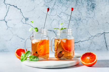 Traditional iced tea with orange and mint and ice in mason jars . refreshing summer drink on white marble board の写真素材