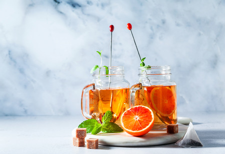 Traditional iced tea with orange and mint and ice in mason jars . refreshing summer drink on white marble board の写真素材