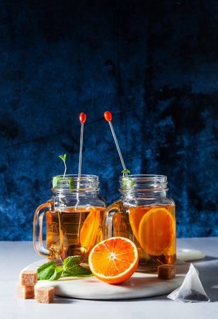 Traditional iced tea with orange and mint and ice in mason jars . refreshing summer drink on white marble board の写真素材