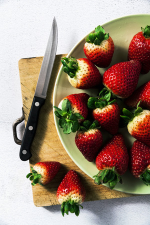 a pile of fresh juicy ripe strawberries on a cutting board and a knife. making a snack or dessert. concept of summer and vitaminsの写真素材