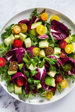 summer bright fresh salad of cherry tomatoes, avocado and radicchio leaves on a white marble table. concept of healthy eating. の写真素材