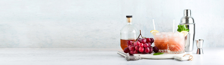 banner with copy space of pink alcoholic cocktail of fresh ripe grapes in a shaker with ice, lemon and mint. summer refreshing drink on the tableの写真素材