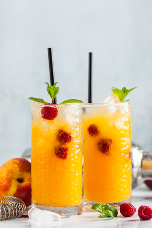 two refreshing drinks from peach juice and raspberries with fresh mint in tall glasses on a marble table with a shaker and bar accessories.の写真素材