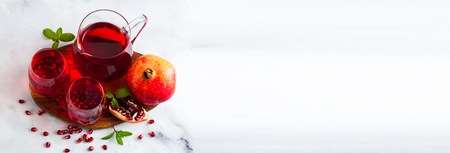 freshly prepared pomegranate juice in a decanter and two glasses on a marble table and a gray stone background with mint leaves and fruit seedsの写真素材