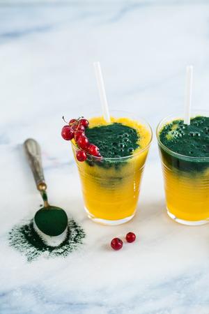 two colored fresh smoothies in glasses with fresh berries. orange banana juice with spirulina powder. detox breakfast. healthy eatingの写真素材
