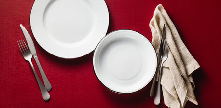 banner of empty dining table set for two. two aluminum plates on a raspberry table with napkins and...