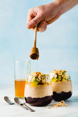 Vegan layered banana dessert of green buckwheat, chia seeds and quinoa with blueberry jam in a glass with fresh fruits, nuts and honey. healthy morning meal for breakfast.の写真素材